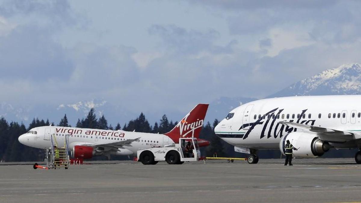 A Virgin America plane takes off past an Alaska Airlines plane waiting to taxi in April at Seattle-Tacoma International Airport in Seattle. Alaska Air Group closed the $2.6-billion acquisition of Virgin America on Wednesday and filed merger documentation.