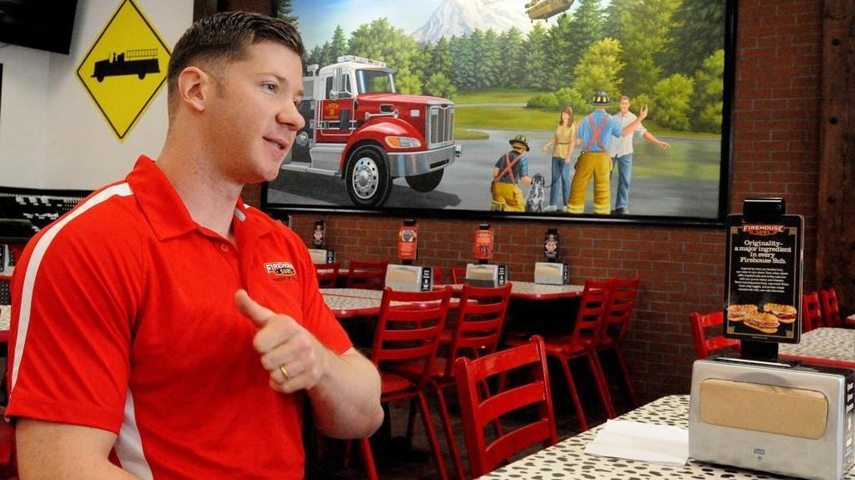 Firehouse Subs’ co-owner Lane Tittle talks about the first responder theme of the Hawks Prairie restaurant he and his wife, Heidi, have opened. The wall mural depicts a Lacey Fire District 3 engine and a JBLM-based Chinook helicopter, with Mount Rainier as the backdrop.