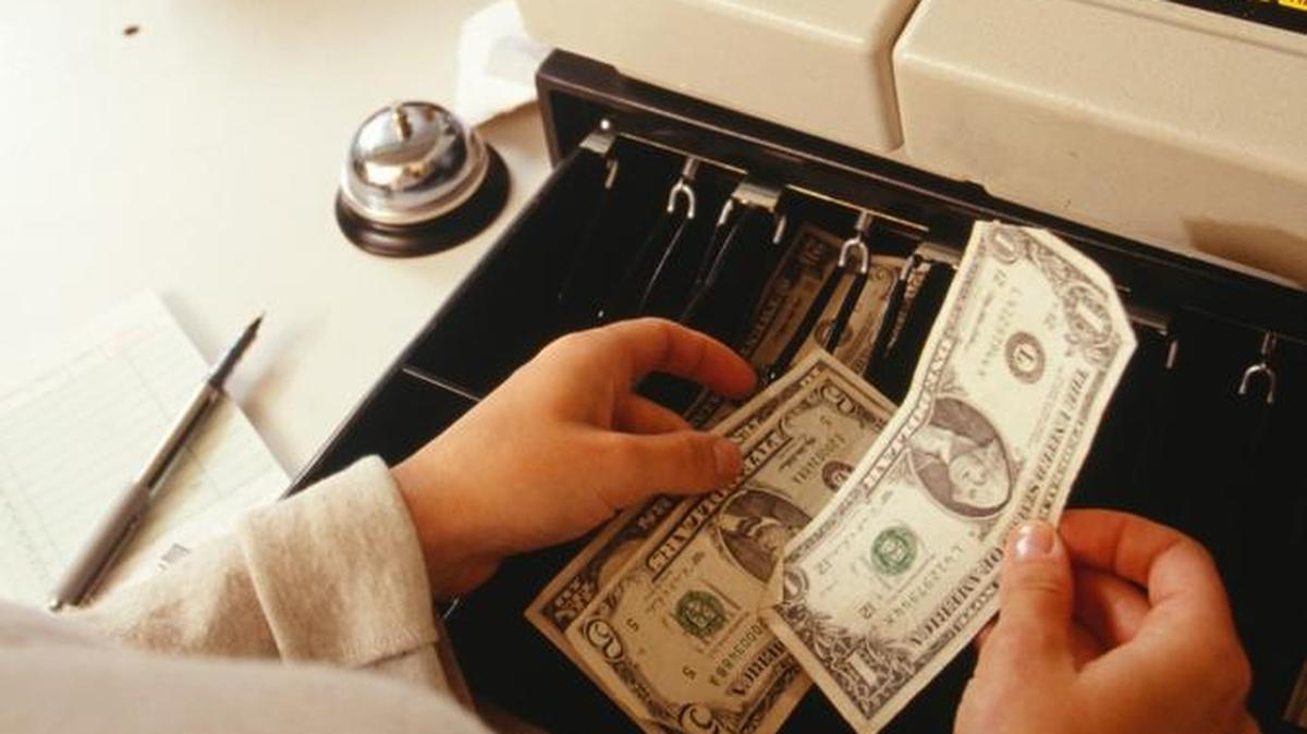 A cashier counts dollar bills for a customer. Next year, California’s statewide minimum will increase to $16.