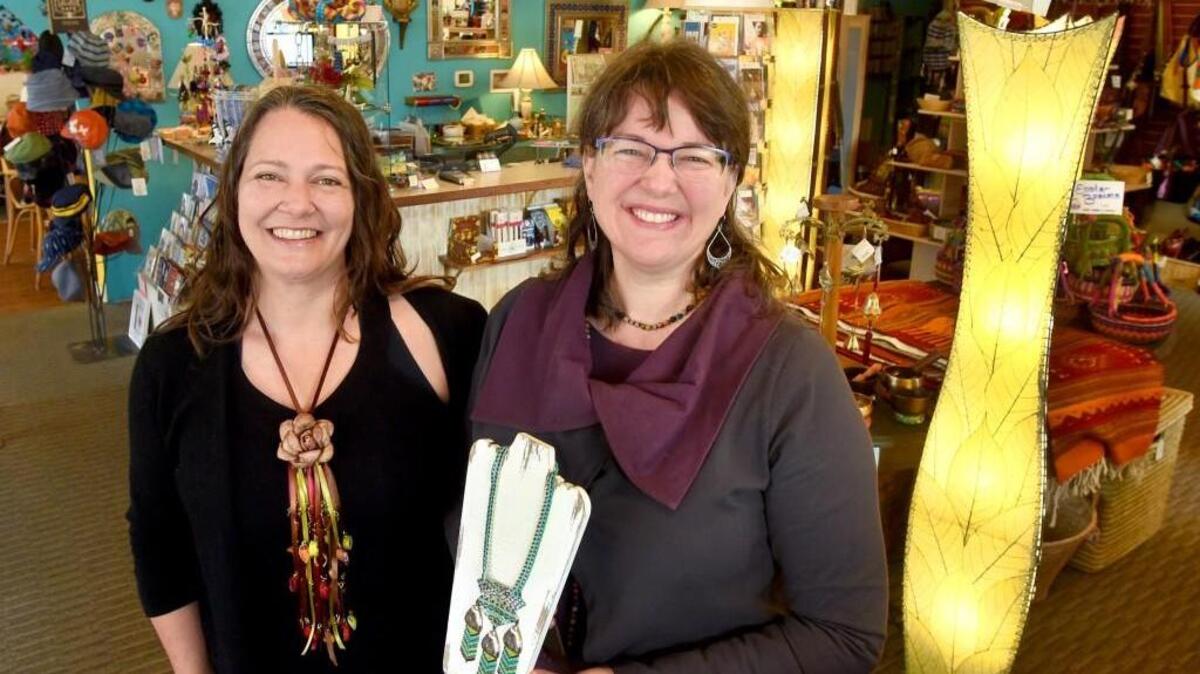 Standing in the New Traditions Fair Trade store, Jody Mackey holds a piece of hand- crafted Huichol Indian jewelry, while co-owner Stacy Muguet wears a silkworm cocoon necklace. Both items are from Mexico.