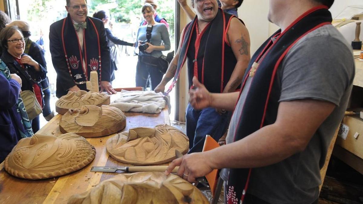 The Evergreen State College President George Bridges, left, watches John Edward Smith and Alexander Stillwater, right, in a carving demonstration during the Fiber Arts Studio Dedication Ceremony at Longhouse Carving Studio on the campus of The Evergreen State College in 2015.