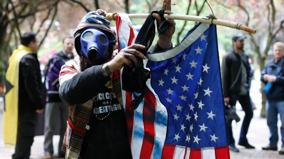 John Durano, who says he flew in from LA to participate and demonstrate his white pride, wears a gas mask and waves an American flag during a demonstration near City Hall and adjacent parks in Portland, Sunday, June 4, 2017. Crowds have swelled to several thousand as demonstrators from varying groups have converged in downtown Portland.