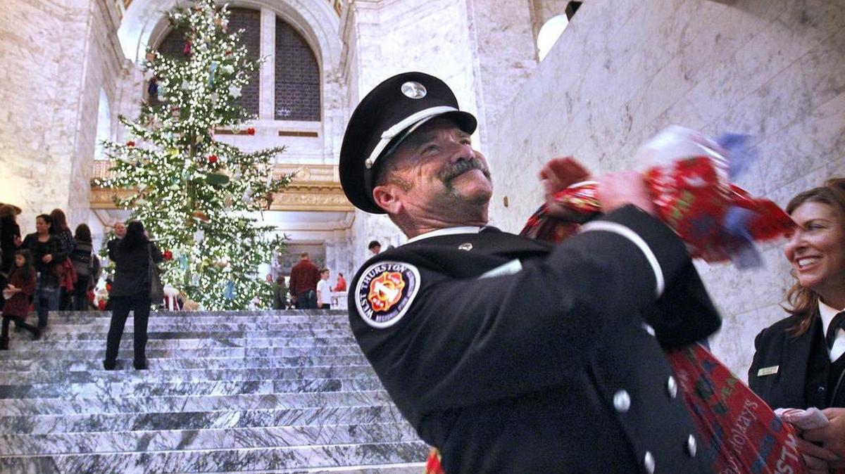 FILE PHOTO: Lt. Robert Maser of the West Thurston Fire District hoists a bag of donated toys as he and Lt. Lanette Dyer (right) head out following the Association of Washington Business' annual Holiday Kids Tree lighting ceremonies in the Capitol Rotunda in Olympia in 2014.