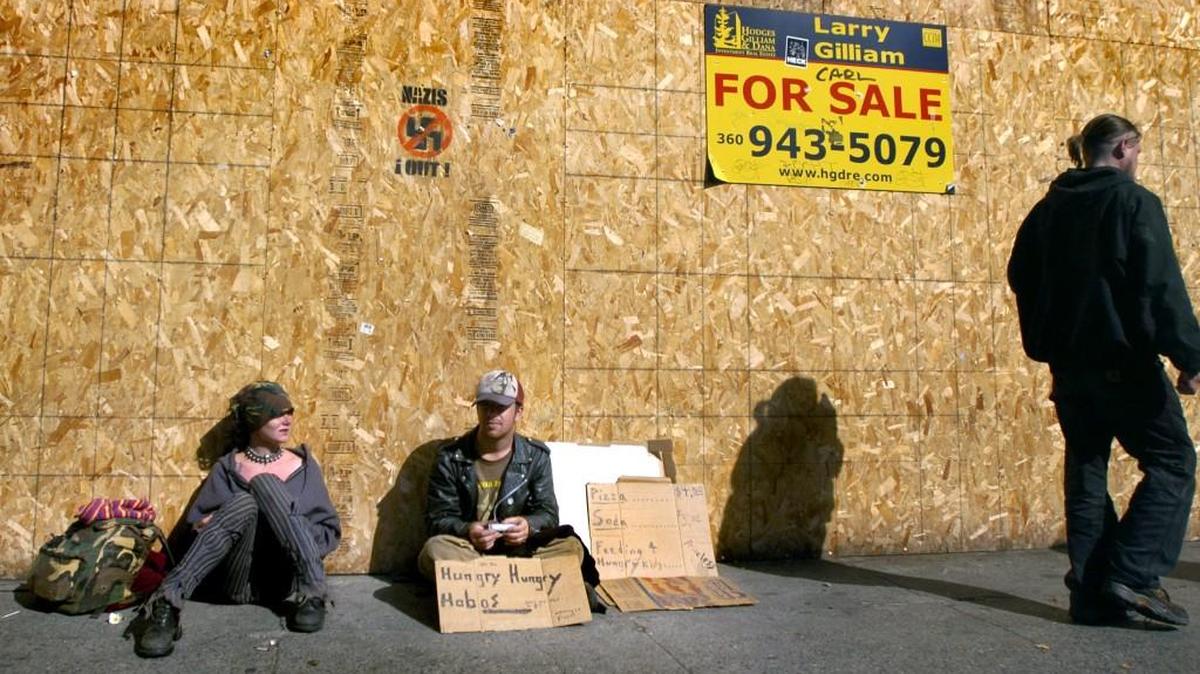 Holding a sign that reads "Hungry, Hungry, Hobos," people who gave their names as Turtle (left) and Lost (right) panhandle in front of an empty storefront along Fourth Avenue in 2006.