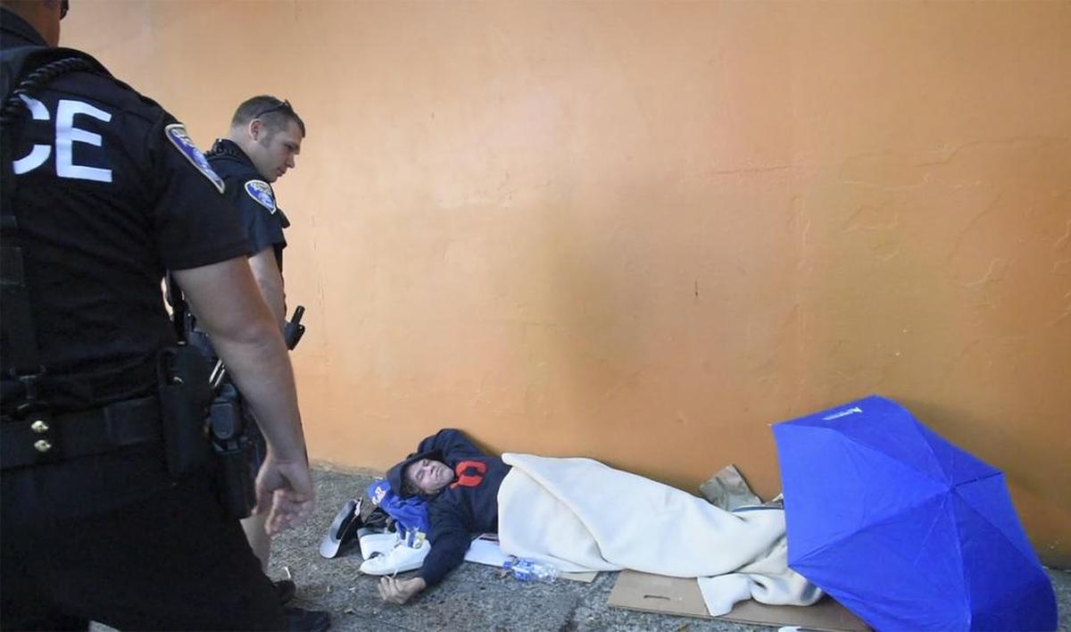 Walking patrol officers Sean O’Brien, center, and Josh Marcuson wake up a man sleeping on Washington Street Northeast.