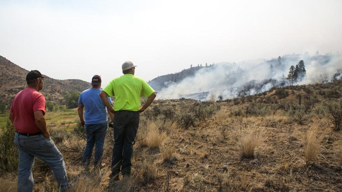 
Brian MacLean, left, of Okanogan, Jeff Demmitt of Omak and Pat Harris of Omak keep an eye on wildfire creeping toward a friend’s near Omak on Friday.
