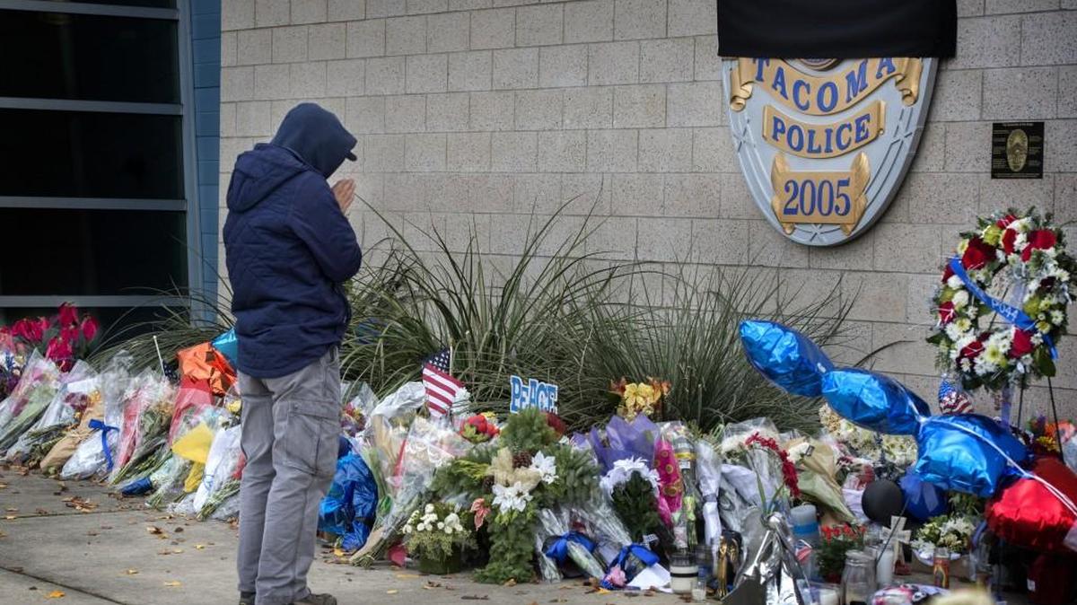 A resident pays respect with a prayer Thursday for fallen Tacoma Police officer Reginald “Jake” Gutierrez at a memorial with flowers in front of the Tacoma Police headquarters.