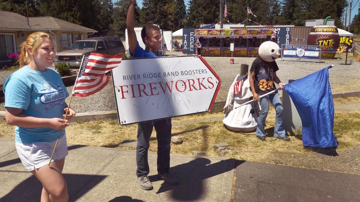 Waving a sign to grab the attention of passing motorists Tuesday afternoon, River Ridge senior Darius Palmer is joined by bandmates Laurel Ponce and David Rosario, both juniors, as they work the corner along Martin Way in front of the school band's fireworks stand. Palmer said the stand will be open until 11 p.m. Wednesday.
