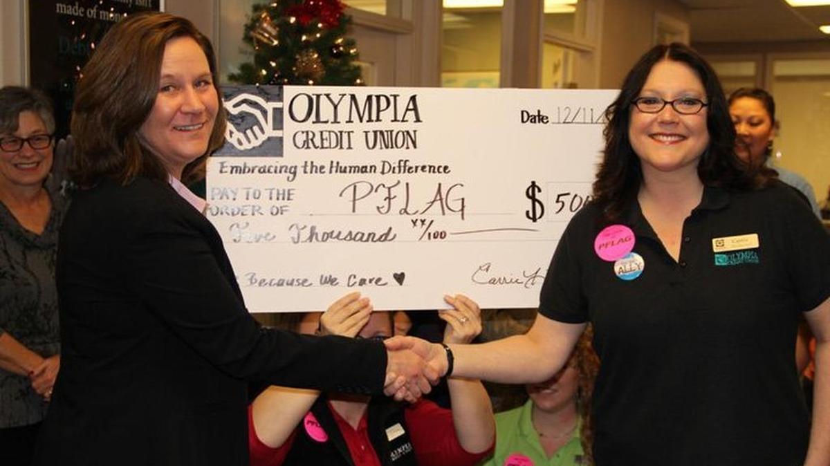 PFLAG Olympia board president Dana McCormick, left, accepts a check for $5,000 from Olympia Credit Union loan supervisor Carrie Hartman during a gathering Dec. 11.