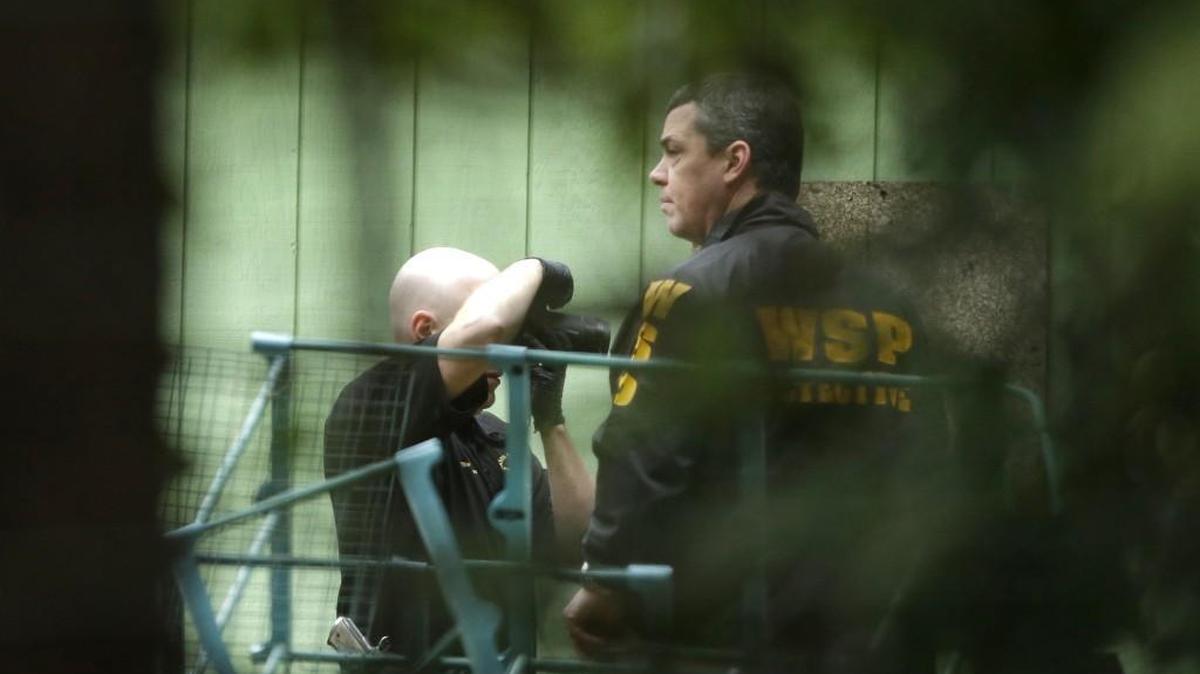 Investigators are seen through trees as they photographs the scene of a fatal shooting Friday near Belfair. A man called authorities on Friday to say he shot his family, leading to an hourslong standoff at a home that ended with the man’s suicide, authorities said.