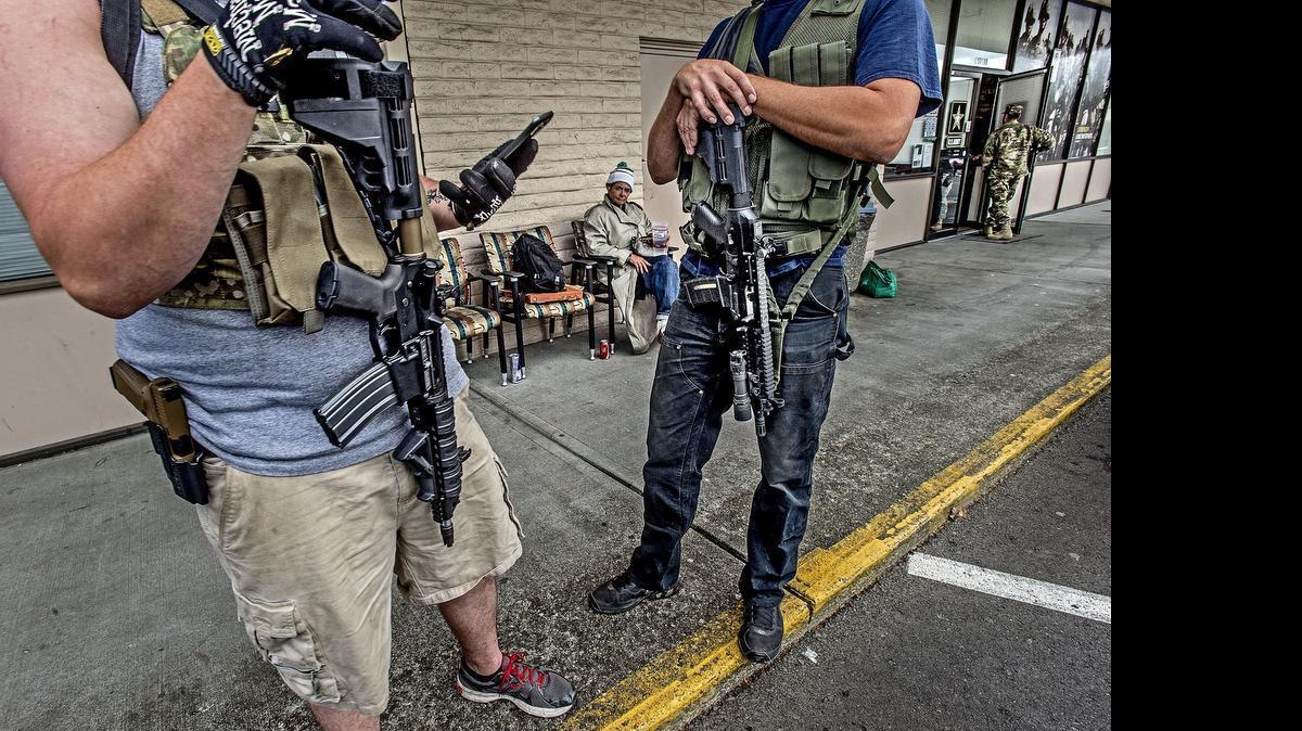 
Zach, 27, left, and his good friend Matt, 34, stand outside the U.S. Army Recruiting Office on 16204 Pacific Ave. South, Spanaway, carrying AR-15 rifles and holstered semiautomatic handguns. Zach said he called the office earlier in the morning to ask if it would be all right for them to come out. He said they are there because of the shooting at another recruiting office in Chattanooga, Tennessee, that left five service members dead. Deanna Rine, seated behind, said "it is all right with me that they are here posing for pictures with their guns." Rine was just hanging out in front of the recruiting office. 
