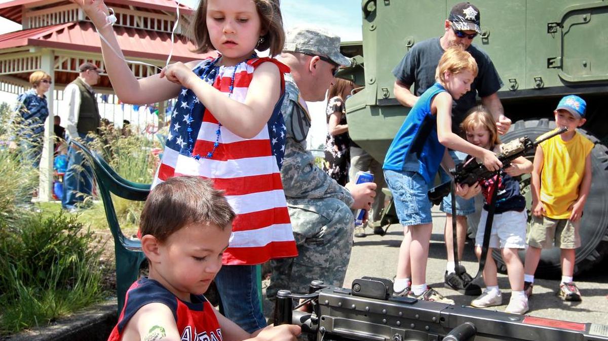 Joseph Switzer, 5, checks out a M2 .50 caliber machine gun, lower left, while others attending the 2012 Armed Forces Day hold a M4 carbine rifle, background, at JBLM. Savannah Weinman, 6, second from left, waits her turn at the machine gun and Sgt. Cory Hall, third from left, supervises.