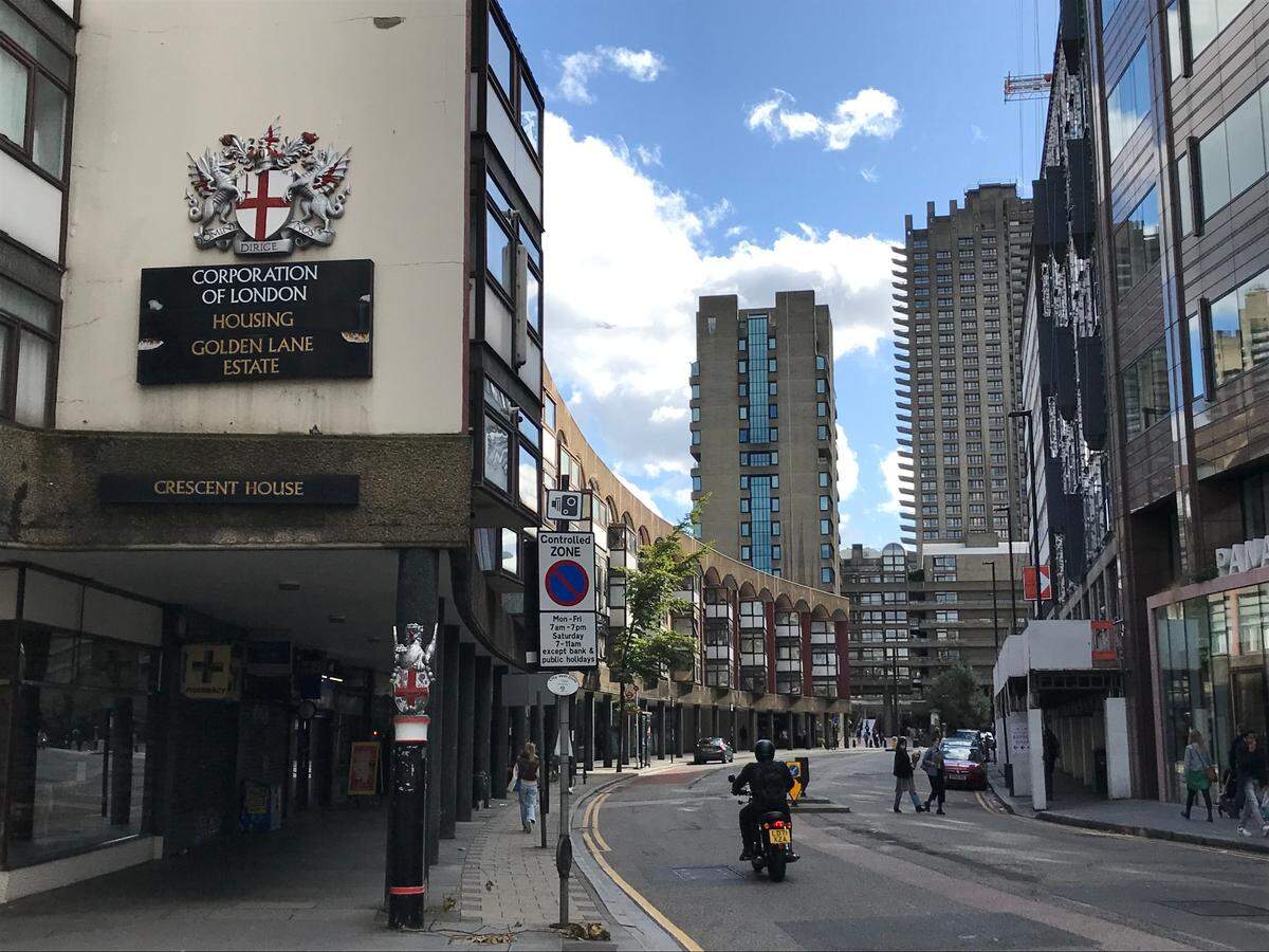 In the foreground: Golden Lane, an early public housing estate built in the 1950s. In the distance: residential towers rise from the Barbican, a multi-use public arts center built in the 1970s by the Corporation of London, the governing entity of the two-square mile city center – but as a moneymaking venture, to be rented at market prices to urban professionals.