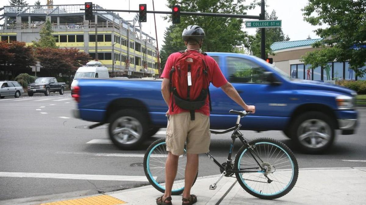 A bicyclist waits to cross College Street at Sixth Avenue in Lacey.