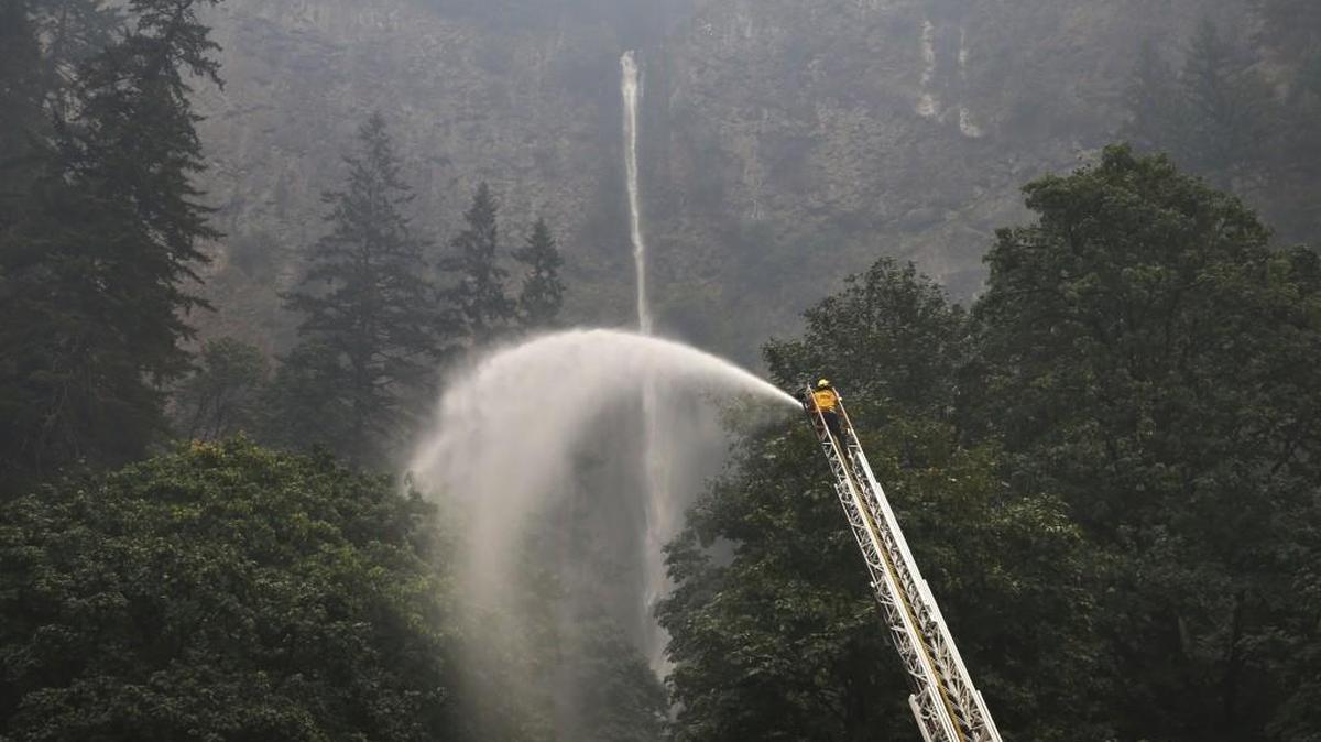 A firefighter maintains a spray of water on the trees around Multnomah Falls on Wednesday as the Eagle Creek Fire continues to burn east of Troutdale, Oregon.