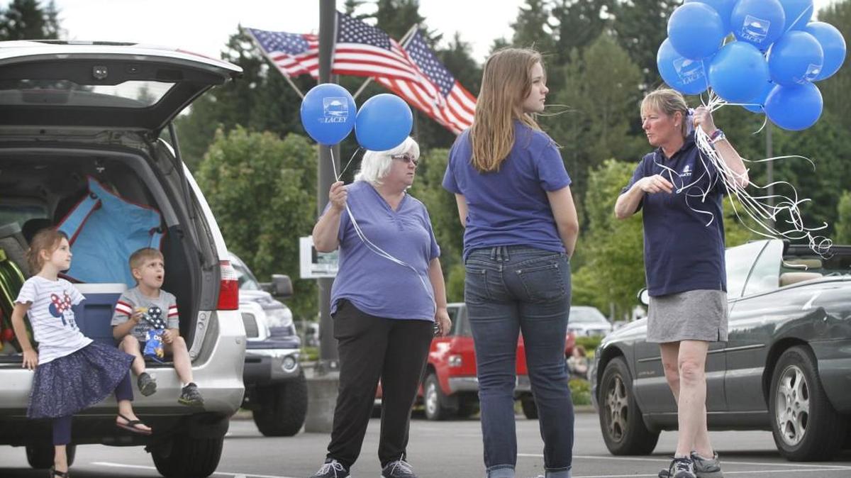 Lacey community liason Mary Coppin (right) offers helium balloons to Laura Scheffer of Lacey and her grandchildren (from left) Serenity Driskill, 5, Corbin Driskill, 6, and Jaden Scheffer, 12, as they wait for the City of Lacey's annual July 3rd fireworks in the parking lot of the Lacey Crossroads Shopping Center on Thursday, July 3, 2014. Lacey’s fireworks display is the first of the holiday weekend.