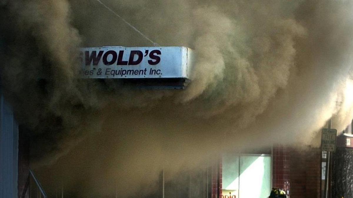 A firefighter pulls a hose as smoke billows from inside Griswold’s Office Supply & Equipment in downtown Olympia on July 31, 2004.