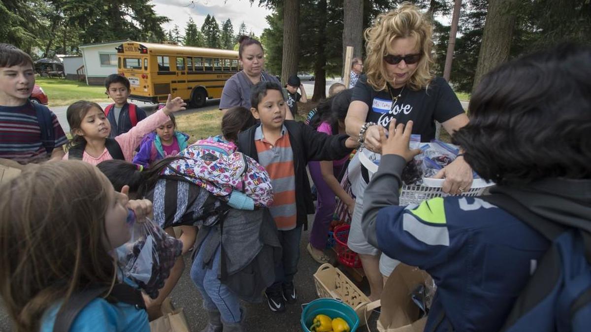 Cathy Kapan of Capital Christian Center is swarmed by kids as they arrive for the Union Gospel Mission's “VegOut” fresh fruit and vegetable giveaway at Rainier Vista Mobile Home Park in Lacey on Friday.