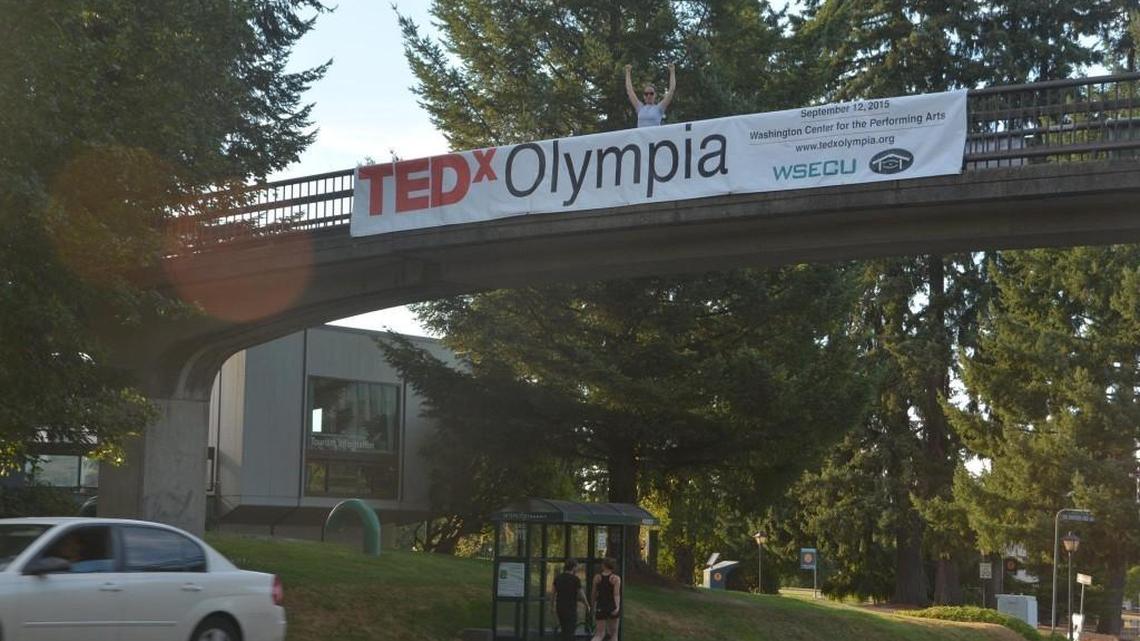In this 2015 file photo, Meg O’Leary, organizer for the first TEDx Olympia, stands with a banner for the event on a bridge over Capitol Way.