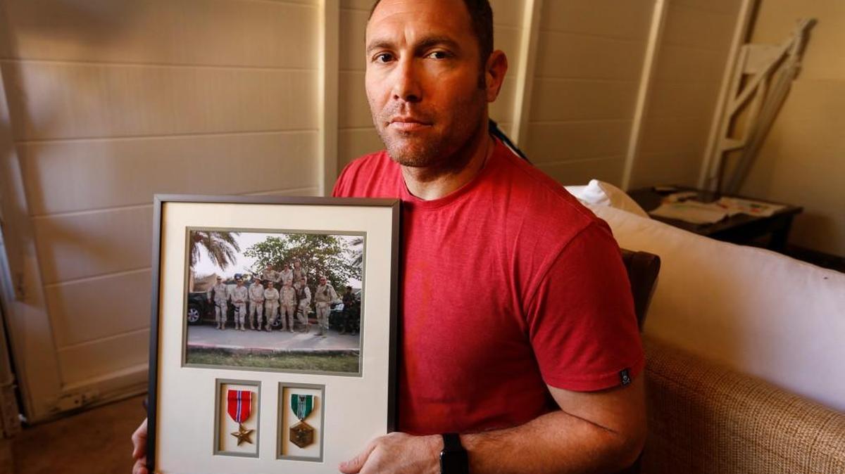 Robert D’Andrea, a retired Army major and Iraq war veteran, holds a frame with a photo of his team on his first deployment to Iraq on Friday, Oct. 21, 2016 in his home in Los Angeles. Nearly 10,000 California National Guard soldiers have been ordered to repay huge enlistment bonuses a decade after signing up to serve in Iraq and Afghanistan. The Pentagon demanded the money back after audits revealed overpayments by the California Guard under pressure to fill ranks and hit enlistment goals.