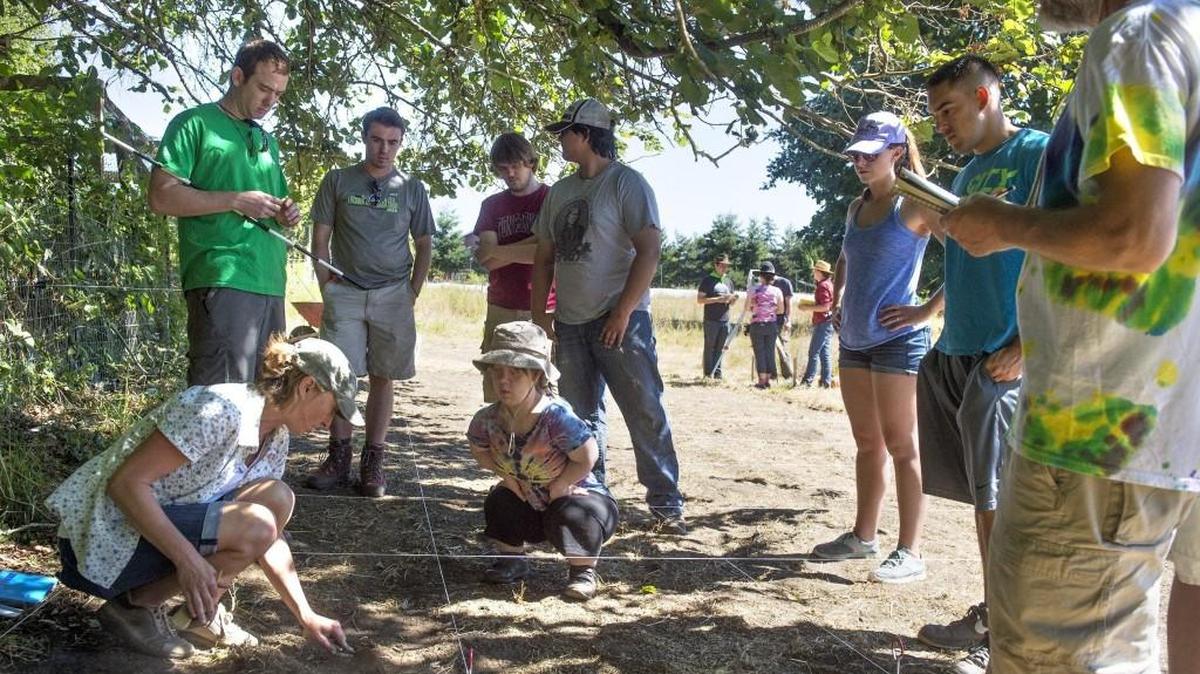 File photo: Instructor Ulrike Krotscheck (lower left) demonstrates excavating technique for students from The Evergreen State College as they set up plots on an archeological dig on the George Bush homestead site in Tumwater last summer.