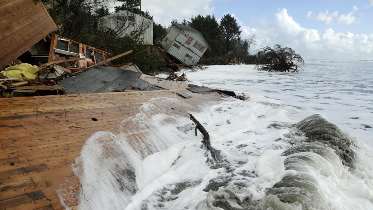 FILE - In this Dec. 12, 2014, file photo, waves break on the remains of a structure as a house that toppled over the eroding Pacific Ocean shoreline of North Cove, Wash., is shown in the background. A new report released Monday, July 30, 2018, provides the most detailed projections for how fast sea levels are expected to rise along Washington state shorelines over the next decades. (AP Photo/Ted S. Warren, File)