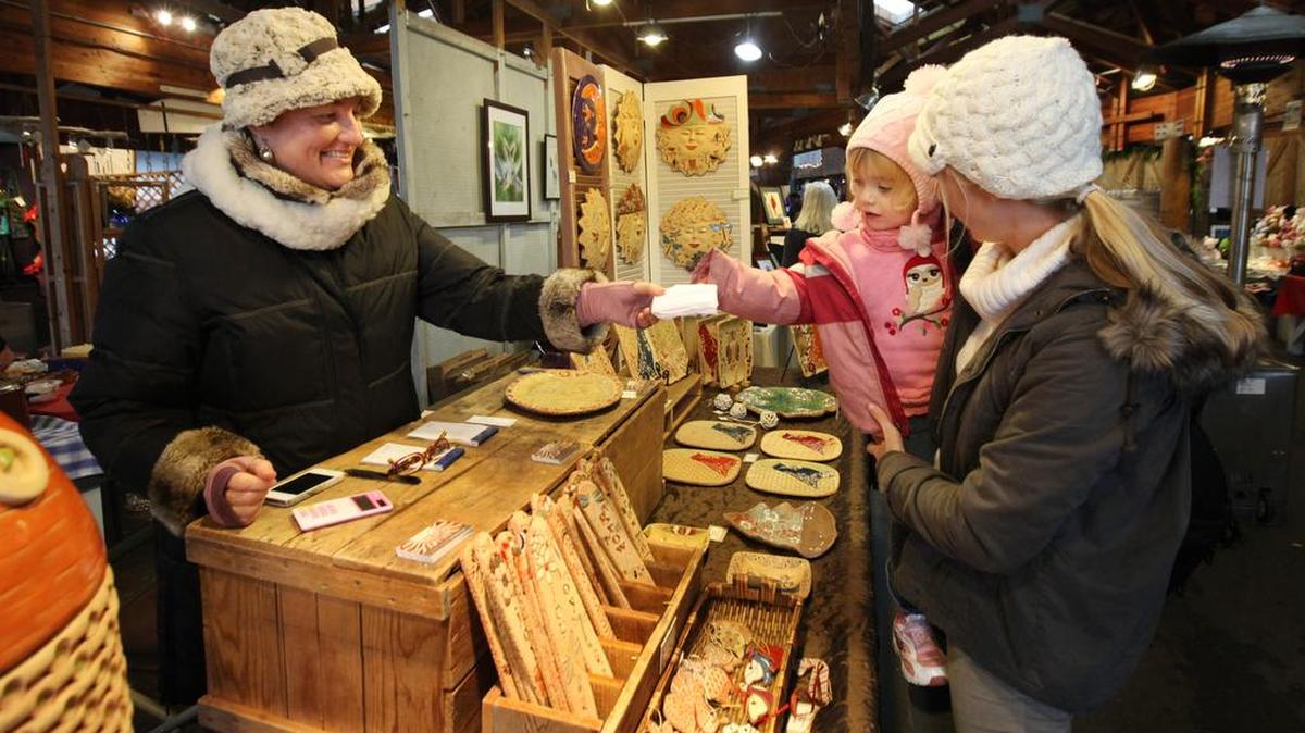 On the final shopping day for the Olympia Farmers Market in 2012, 2-year-old Lauryn Harris receives a small Christmas Eve present from ceramic artist and market vendor Marion Pollmann while in the arms of her mother, Katie. The market is again open Monday for last-minute holiday shopping.