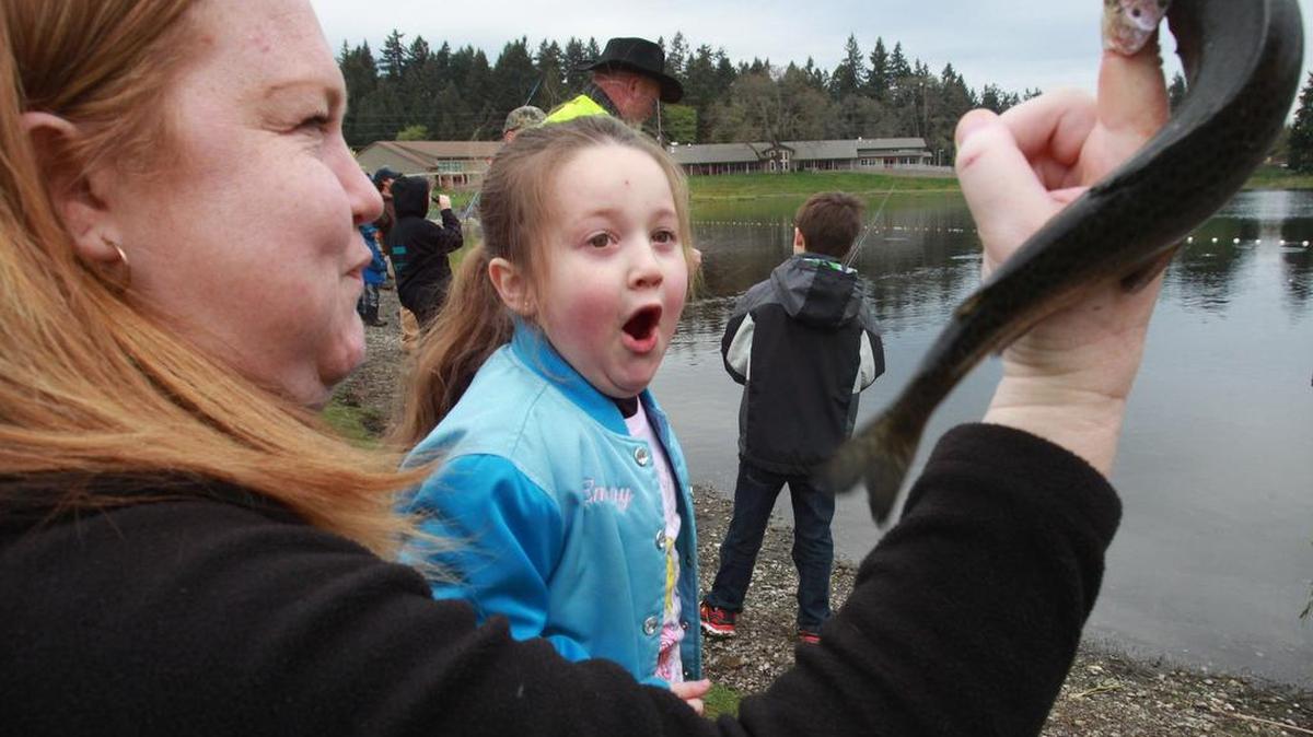 Emeory Palmer, 5, watches as her mom, Jamie Palmer of Lacey, shows her how to hold the rainbow trout she caught during the 2014 Lacey Family Fish-In at Long's Pond. The Fish-In returns on Saturday.