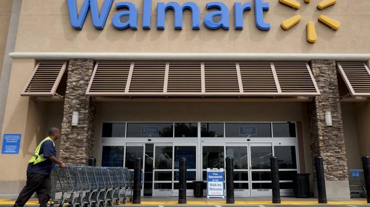 A worker pushes shopping carts in front of a Walmart store in La Habra, Calif.