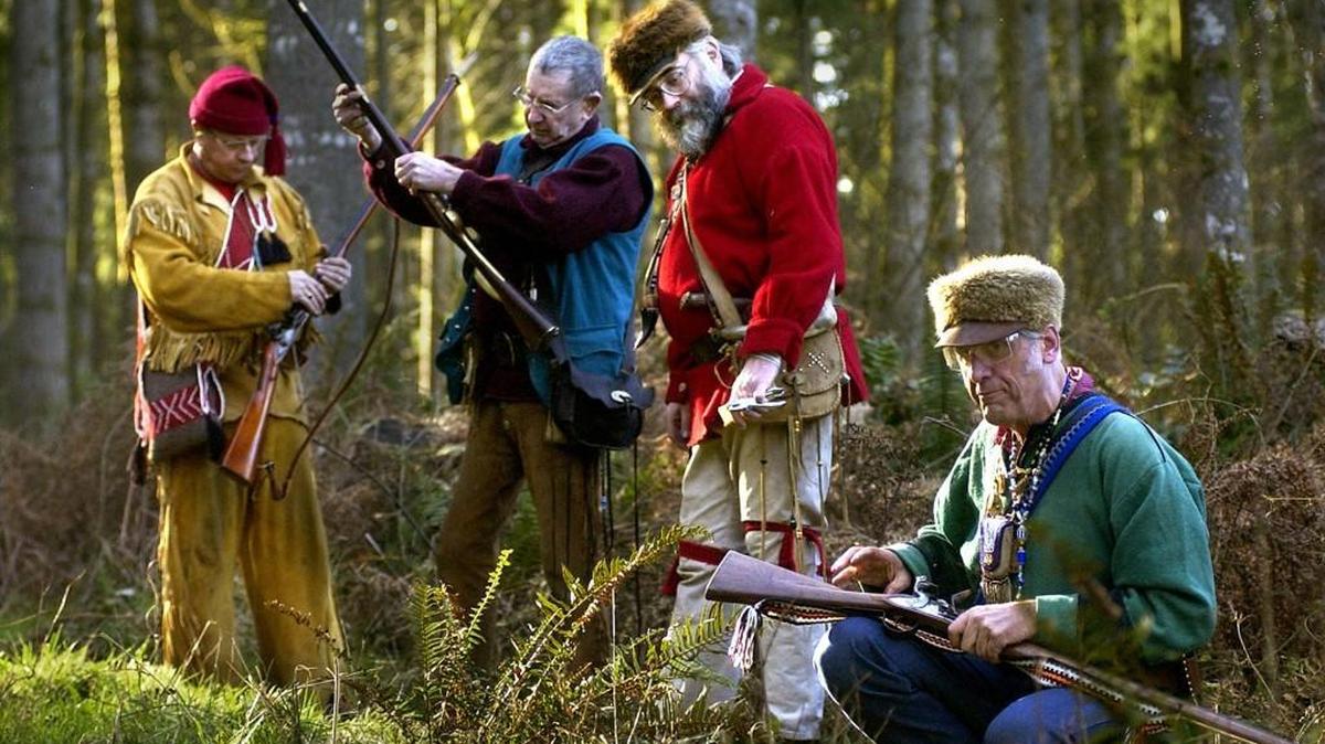 In costumes reminiscent of the clothing worn by trappers in the fur trade era , participants (from left) Tim Sampson of Tenino, Harold Moore of Olympia, Steve Skillman of Yelm, and Mike Nesbitt of Olympia reload their trade guns between targets during the trail walk competition at Capitol City Rifle Club's Rain Dee Voo event in Littlerock.