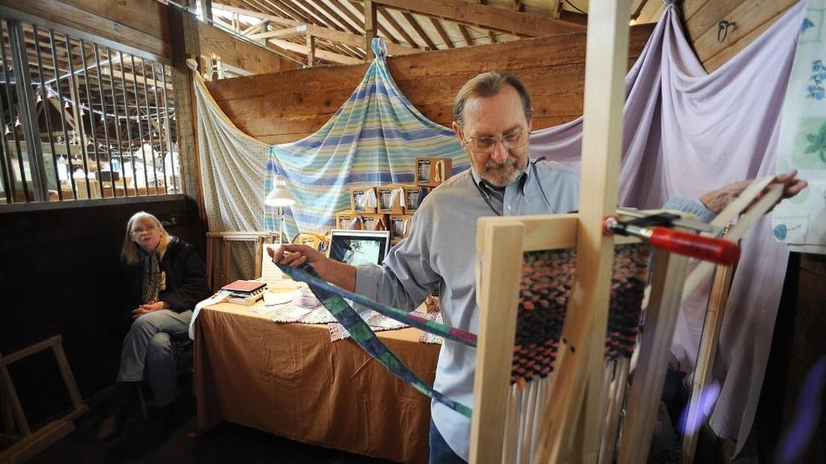 
Settled in one of the Sherman Valley Ranch horse stalls, Burt Gumeson demonstrates one of his rag rug looms while wife Barbara looks on during the weekend Queen Bee French Flea market Sunday. Held in the ranch’s rustic setting, the event featured items ranging from antiques, crafts, clothing and furniture to food.
