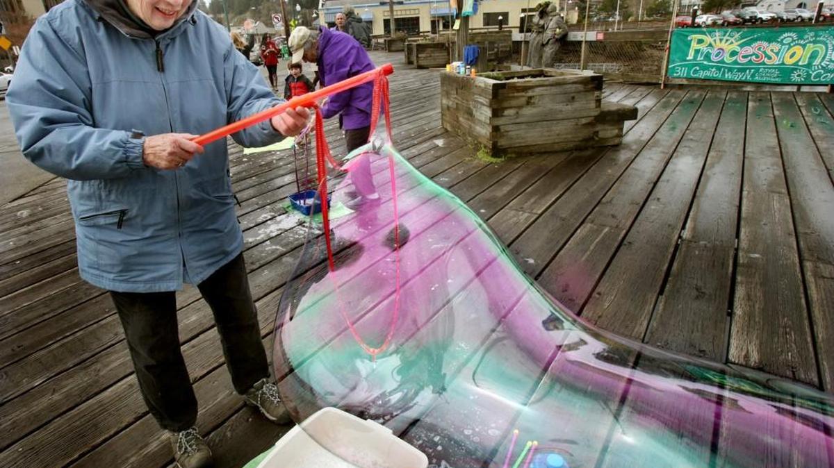 Working against a challenging breeze Gita Moulton creates a colorfully large soap bubble near near the Kissing Statue on Olympia's Percival Landing. She started the annual event 20 years ago with another woman, and attracts participants who stop by to craft their own bubble art. Now in her 80s, Moulton says she's ready to hand her bubble wand off to others to continue the yearly celebration, which is also meant to welcome in the Spring Equinox