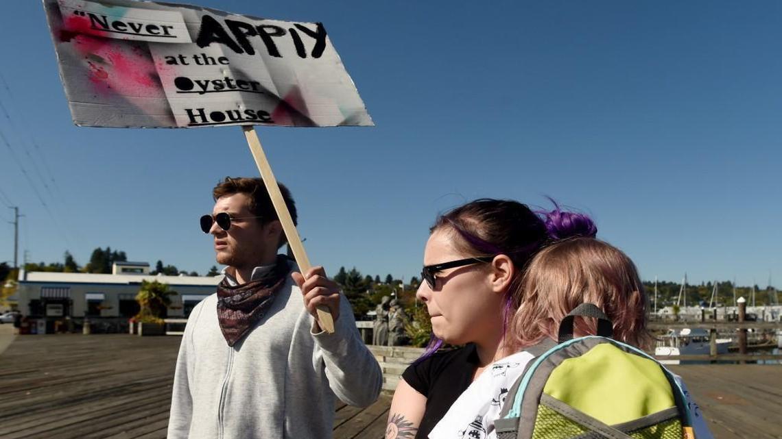Christian Ramirez, a former manager at the restaurant, joined Lexi Paul with her son, Ezra, 3, for a noon demonstration Wednesday along the Percival Landing boardwalk. They were protesting working conditions at the landmark Oyster House, shown in the background.