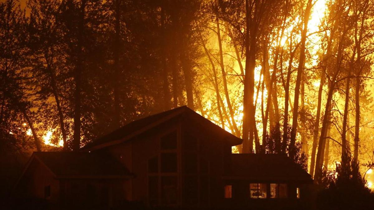 
A wildfire burns behind a home on Twisp River Road on Thursday in Twisp. Authorities on Wednesday afternoon had urged people in the north-central Washington town to evacuate because of a fast-moving wildfire. 
