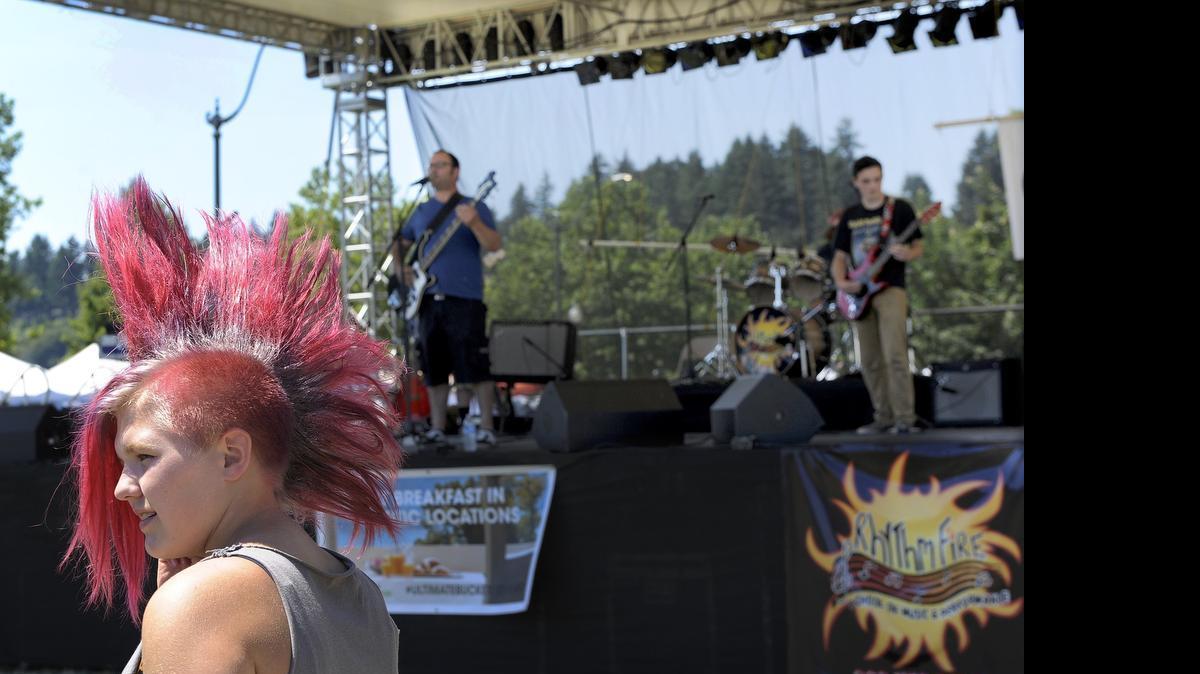 
Sporting a distinctive mohawk hairstyle, 13-year-old Genna Hamlin talks to friends as the band ARK entertains while she awaits her band’s performance during the Rhythm Fire School of Music and Performance Sunday concert on the Capital Lakefair’s closing day of 2015. The Olympia-area music school annually hosts the concert, which features a number of short performances by young musicians from all over the South Sound.
