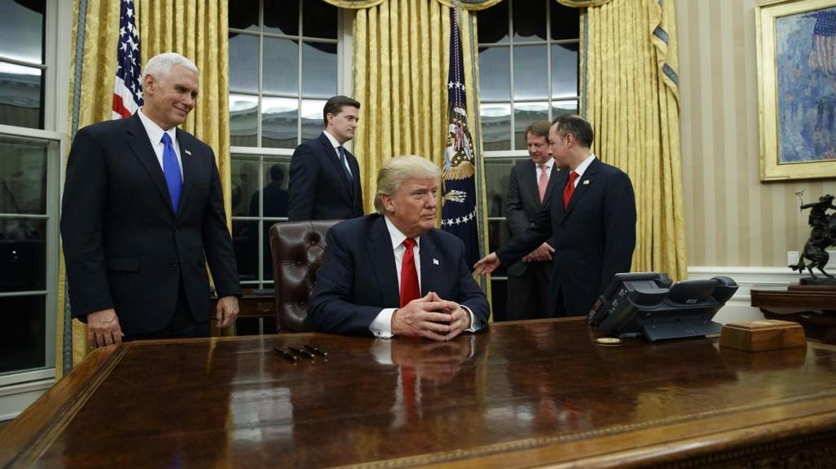 Vice President Mike Pence, left, watches as President Donald Trump prepares to sign his first executive order Friday in the Oval Office of the White House in Washington.