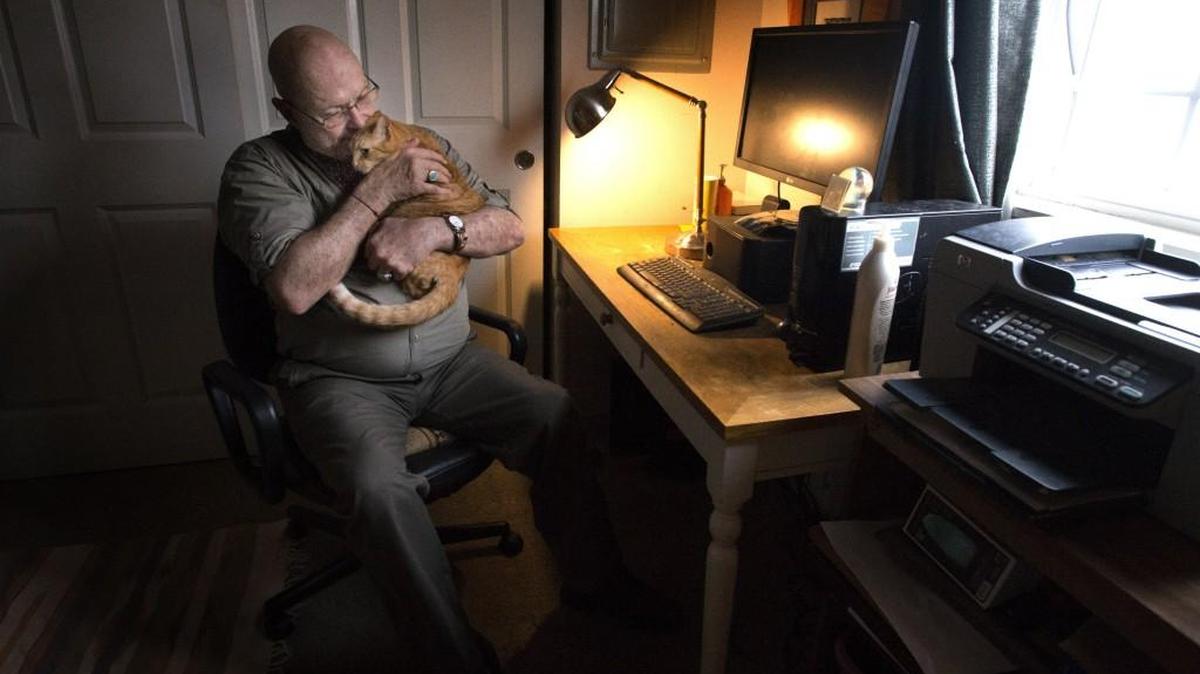 John Hannaman plays with Assie, 1, his orange tabby cat, at his Kent apartment on Monday.