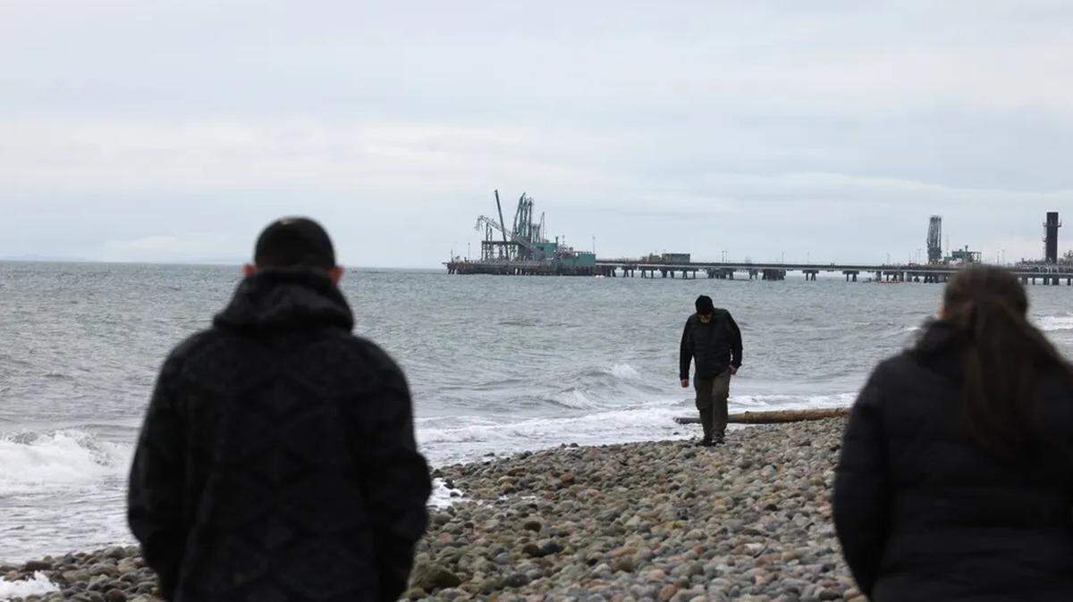 Former Lummi Nation Chairman Jay Julius, left, who lived and breathed the Cherry Point coal terminal fight for years, walks with Councilmember Karlie Kinley on the beach as a dock attached to BP’s Cherry Point Refinery is seen in the distance near Ferndale on Dec. 28, 2023.