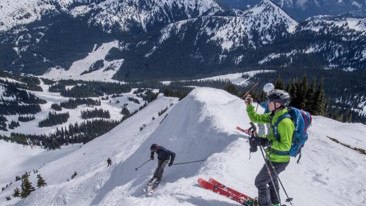 Skiers drop into Powder Bowl on a warm and sunny spring day at Crystal Mountain Resort.