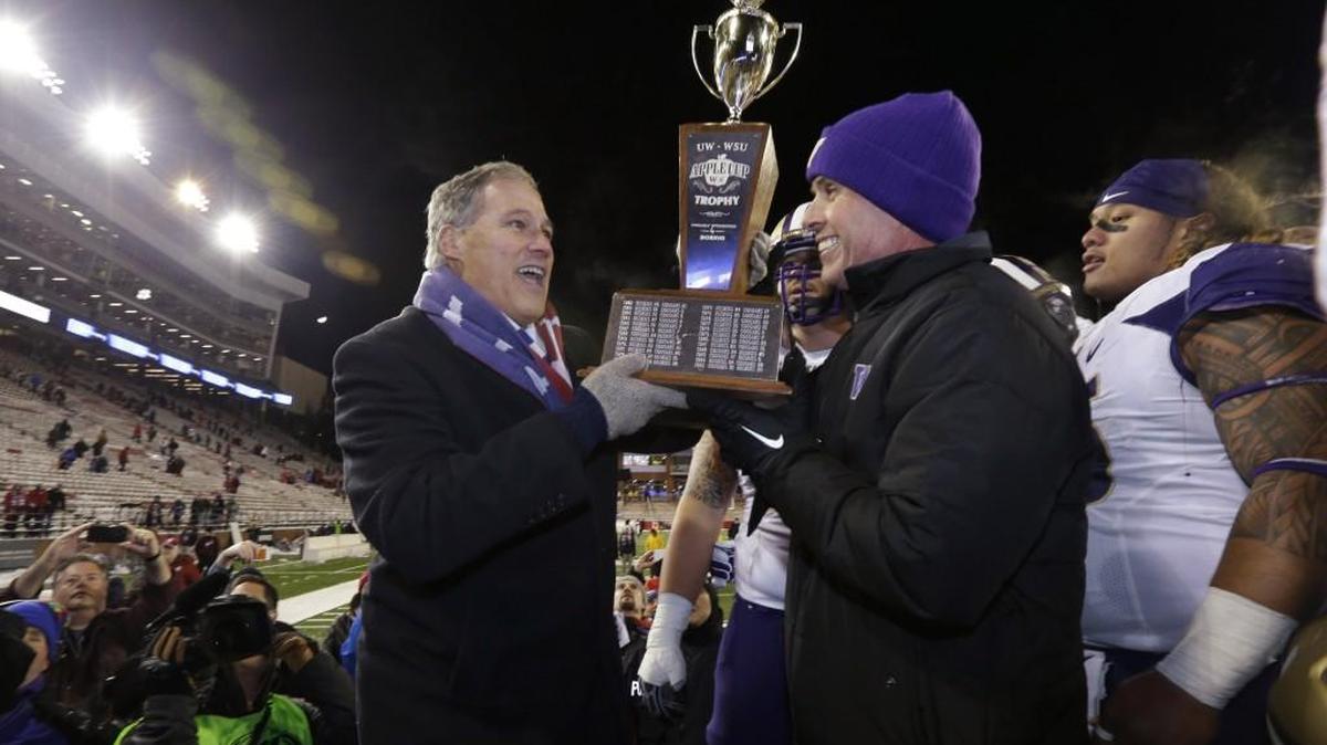 Washington coach Chris Petersen, right, accepts the Apple Cup Trophy from Gov. Jay Inslee on Nov. 29, 2014, after the Huskies defeated the Cougars 31-13 in Pullman.