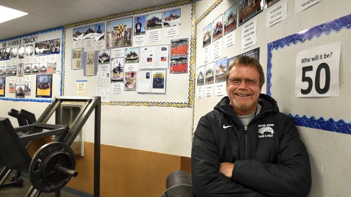 River Ridge track and field coach Phil Lonborg stands next to a wall in the high school’s weight room filled with pictures of the 49 individual state champions he has coached since 1994 with No. 50 still up for grabs. Lonborg has also coached the Hawks to three team state titles.
