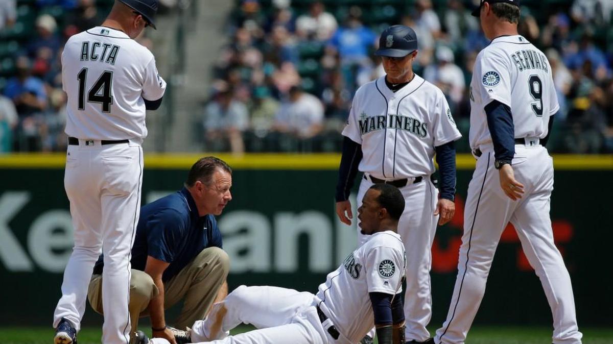 Jean Segura is examined by trainer Rob Nodine in the fourth inning after suffering an injury to his right ankle. Manager Scott Servais and coaches Manny Acta and Casey Candaele look on.