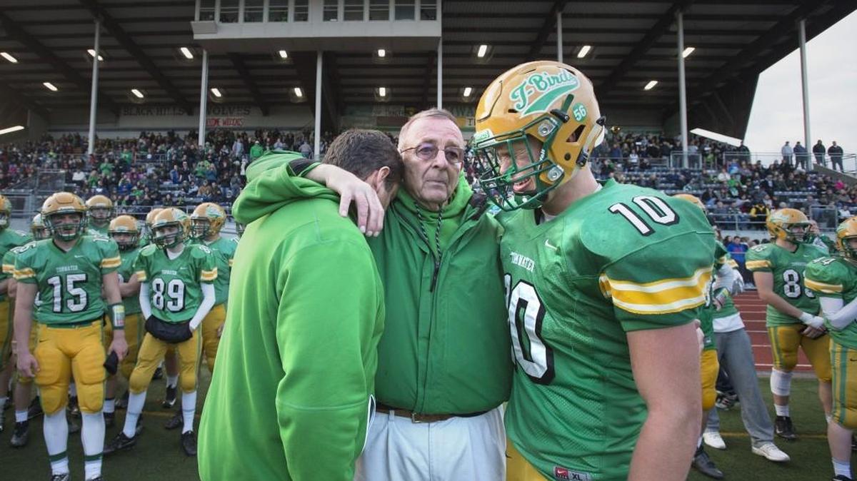 Tumwater High School football coach Sid Otton hugs his son, Tim, and grandson, Cade, as the final seconds of the Thunderbirds’ state-quarterfinal loss to Archbishop Murphy on Nov. 19 at Tumwater District Stadium. Otton retired that day after 49 years of coaching with the most wins in Washington state high school football history. This weekend he’s going to the Pro Bowl in Orlando, Florida.
