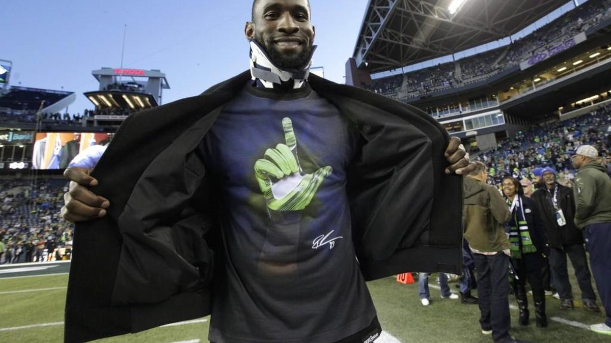 Injured Seahawks wide receiver Ricardo Lockette wears a neck brace and a T-shirt with a team hand signal in the shape of an “L” on the playing surface at CenturyLink Field before Sunday’s night’s game agaisnt Arizona. The “L” stands for “Love our brothers.”