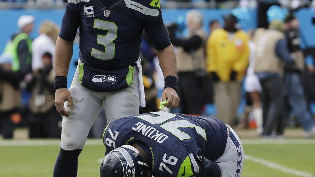 Russell Okung kneeling with a separated shoulder as quarterback Russell Wilson (3) stands over his left tackle in the Seahawks’ season-ending playoff loss at Carolina Jan. 17. Okung emailed teams Wednesday that he was having surgery in advance of his free agency.