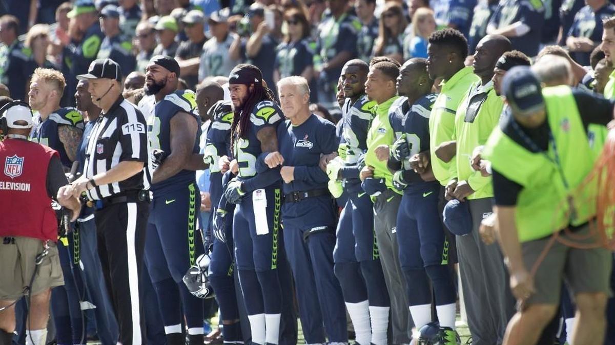 Seahawks corner back Richard Sherman and head coach Pete Carroll stand arm-in-arm with players and staff as they wait for the start of the national anthem before Sunday's NFL season opener against the Miami Dolphins at CenturyLink Field in Seattle on Sept. 11, 2016.