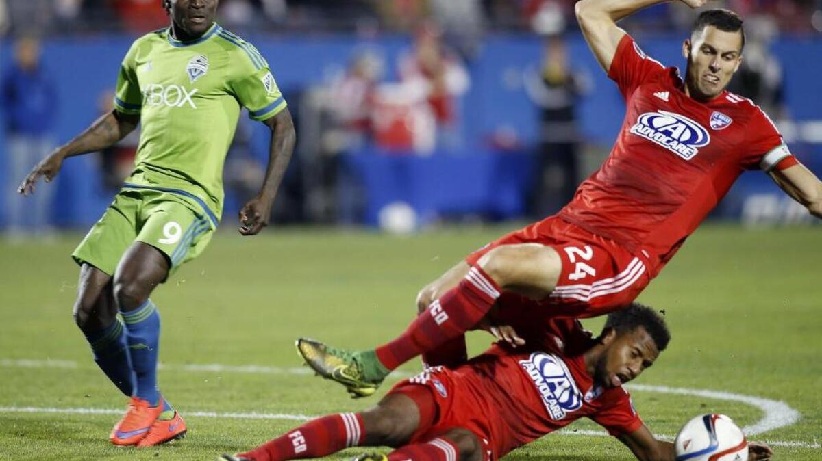 FC Dallas defender Matt Hedges (24) and midfielder Kellyn Acosta, bottom, collide while trying to break up a pass intended for Seattle Sounders FC forward Obafemi Martins (9) during the first half of an MLS soccer western conference semifinal playoff match Sunday in Frisco, Texas.