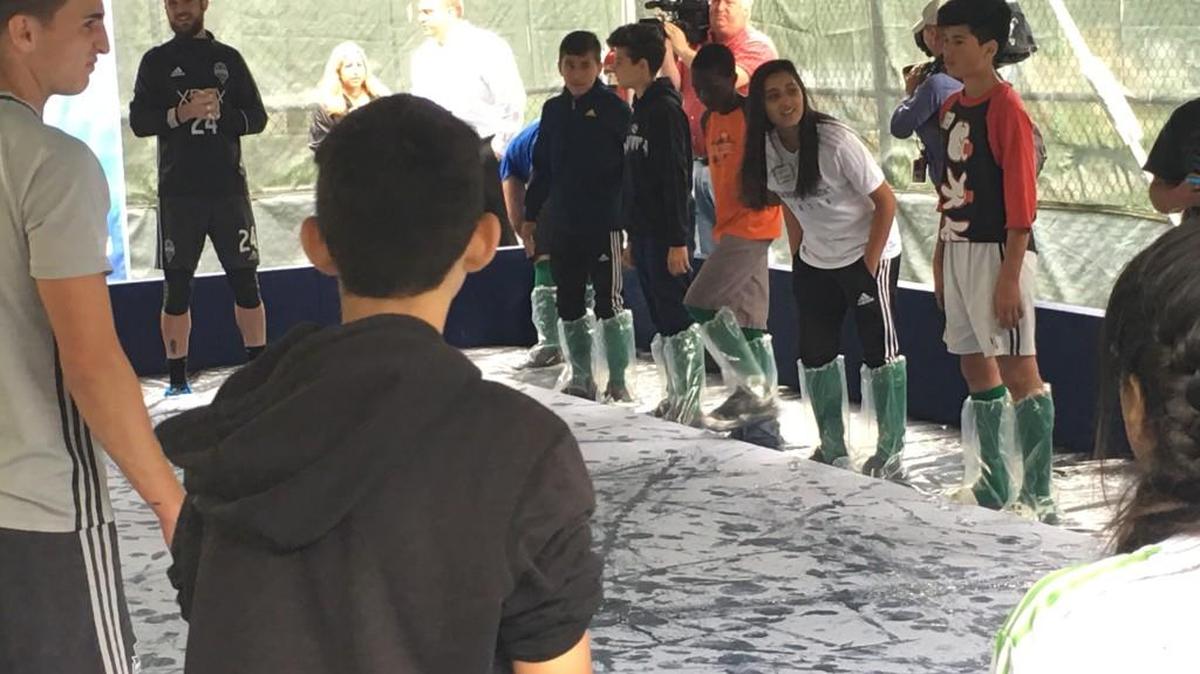 Stefan Frei, rear and facing camera, leads students and teammate Aaron Kovar (left) and Voyager Middle School art students in kicking a painted soccer ball across canvas in the first phase of the ‘Fabric of Sounders FC’ art project that will eventually be displayed at CenturyLink Field.