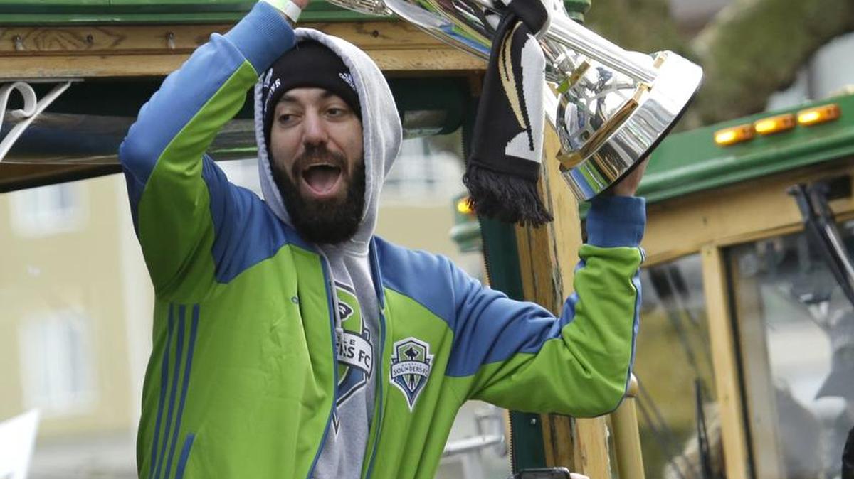Sounders forward Clint Dempsey holds up the the MLS Cup trophy for fans as he rides a trolly with teammates during a celebration march, Tuesday, Dec. 13, 2016, in Seattle. The Sounders defeated Toronto FC on Dec. 10, 2016 to win the MLS soccer championship. (AP Photo/Ted S. Warren)