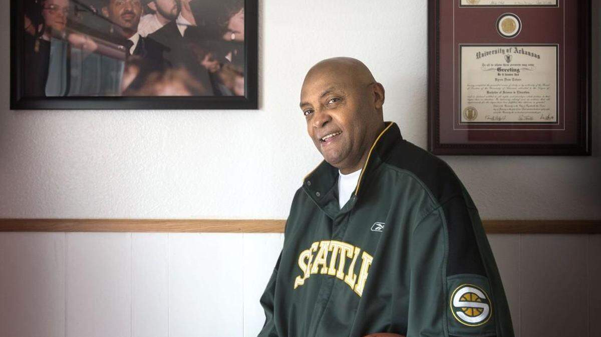 Former Seattle SuperSonics forward Dean Tolson poses at his Tacoma home last year. On the wall is a photo of him during his first graduation from the University of Arkansas in 1988 and his two diplomas from the school. The top diploma is his master’s degree diploma.